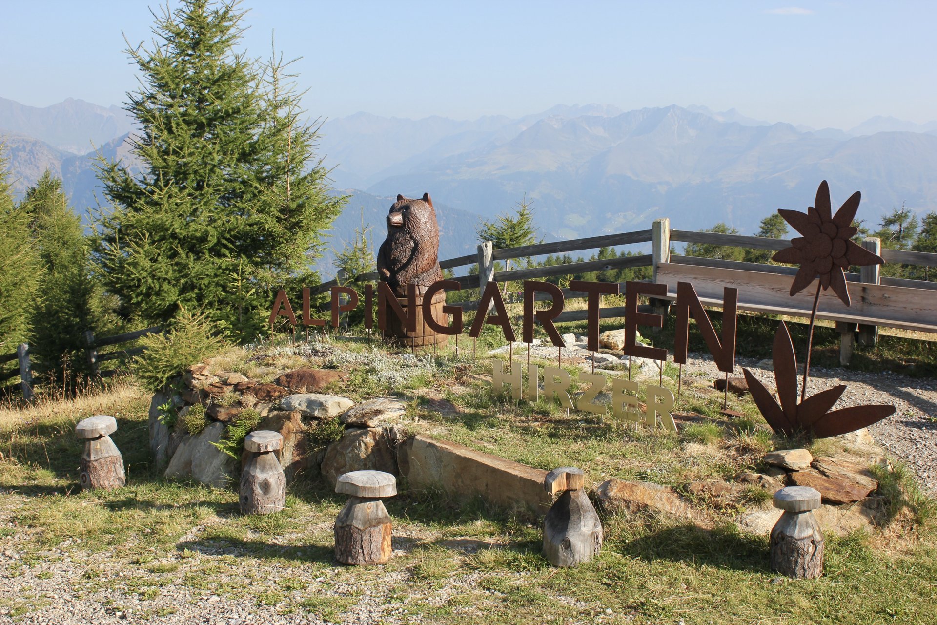 Alpingarten im Hirzergebiet mit Holzfiguren und Bergpanorama