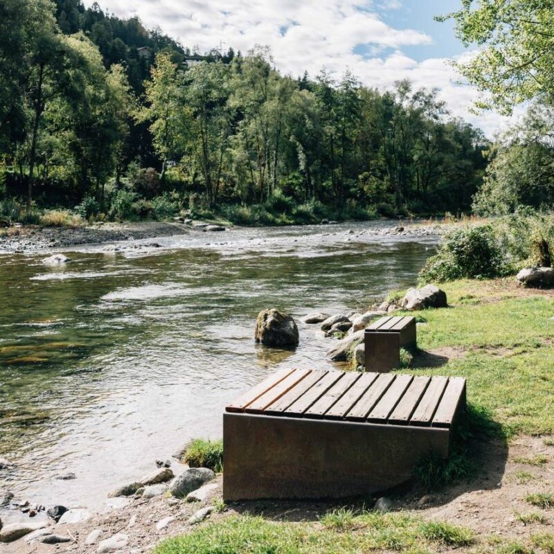 Flussufer mit Steinen, Bäumen und einem hölzernen Sitzplatz