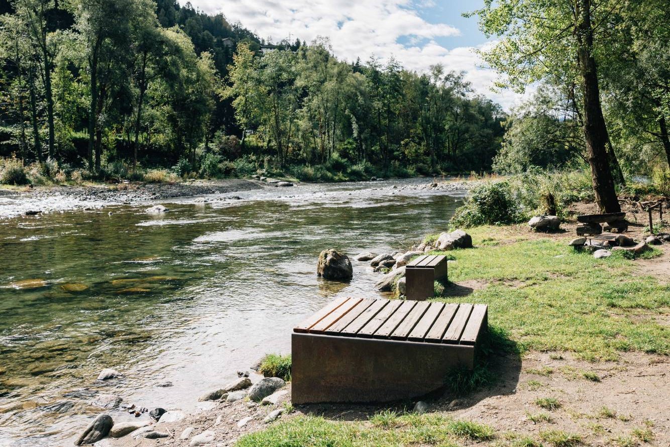 Flussufer mit Steinen, Bäumen und einem hölzernen Sitzplatz