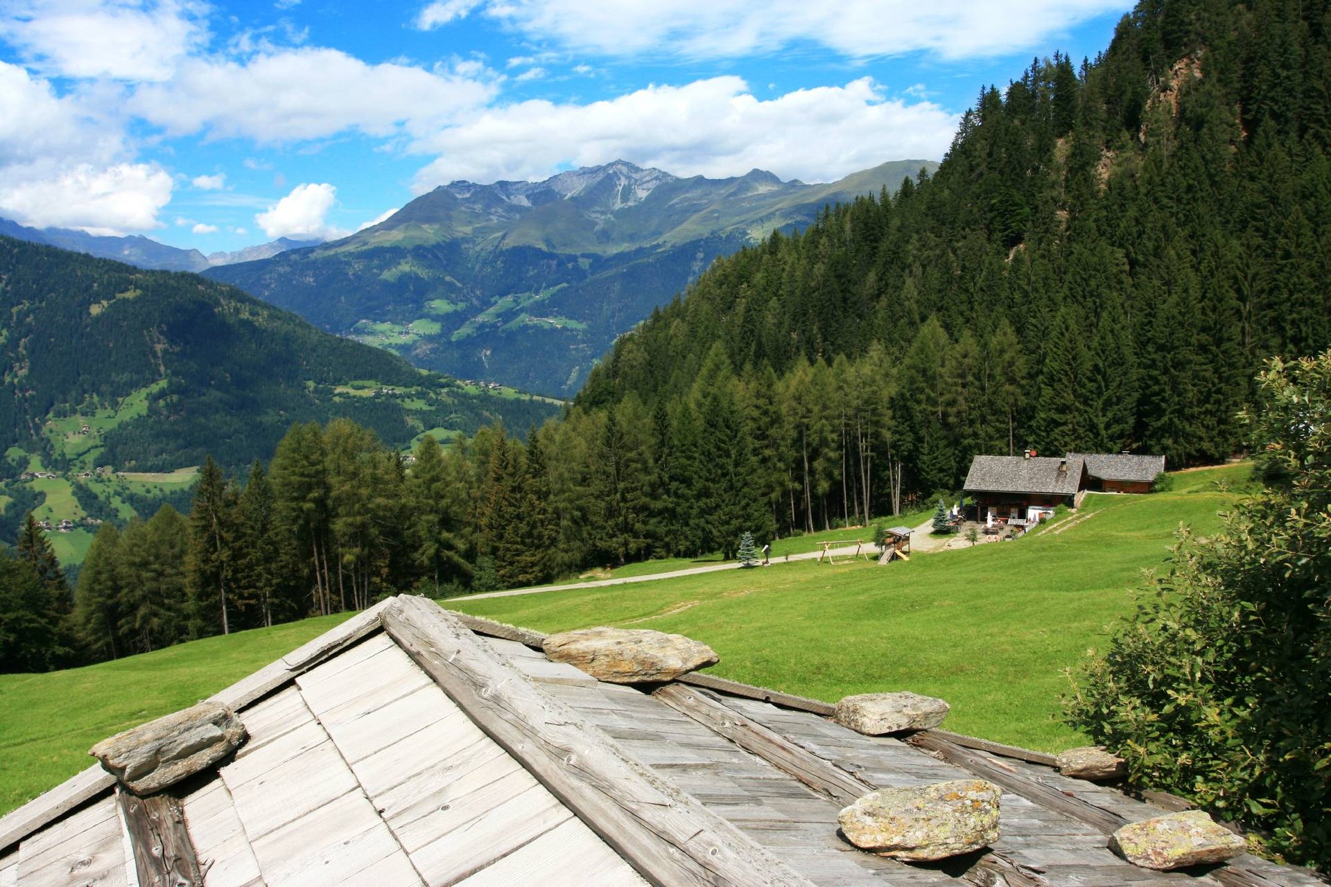 Blick über Holzdächer und Almwiesen in die Berge
