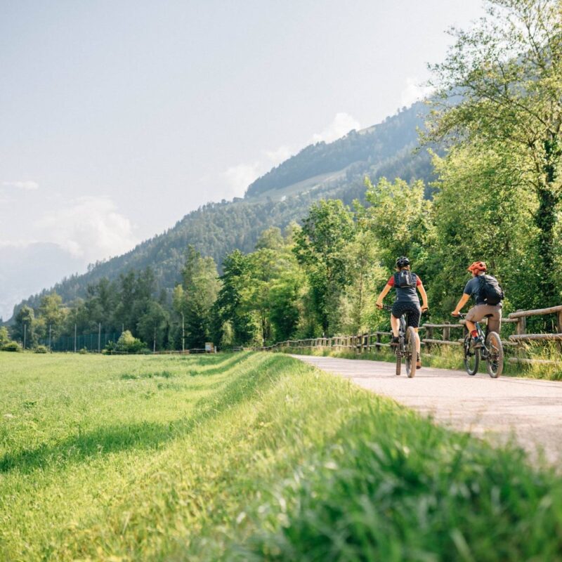Radfahrende auf einem Weg neben einer grünen Wiese im Tal