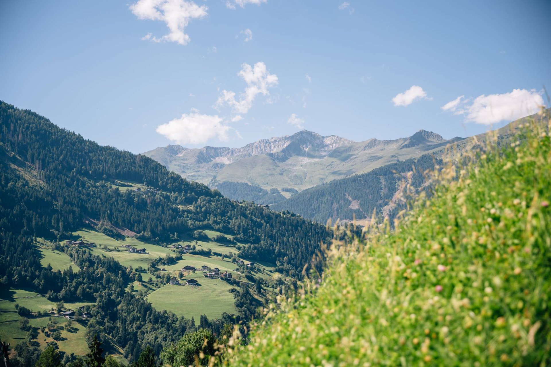 Blick über einen Wiesenhang auf Bergdörfer und Bergketten